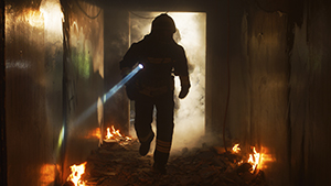 A firefighter with a flashlight explores a smoky, burning hallway