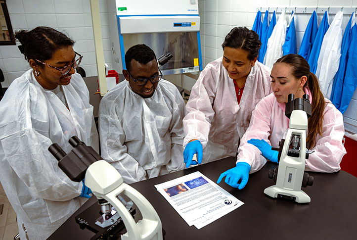 A group of people gather around two microscopes in a lab
