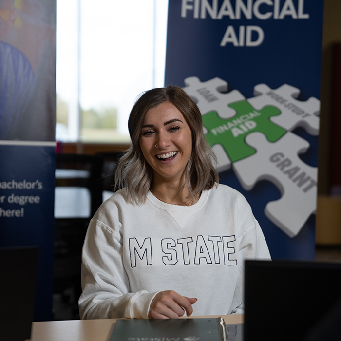 An M State employee sits in front of a financial aid banner