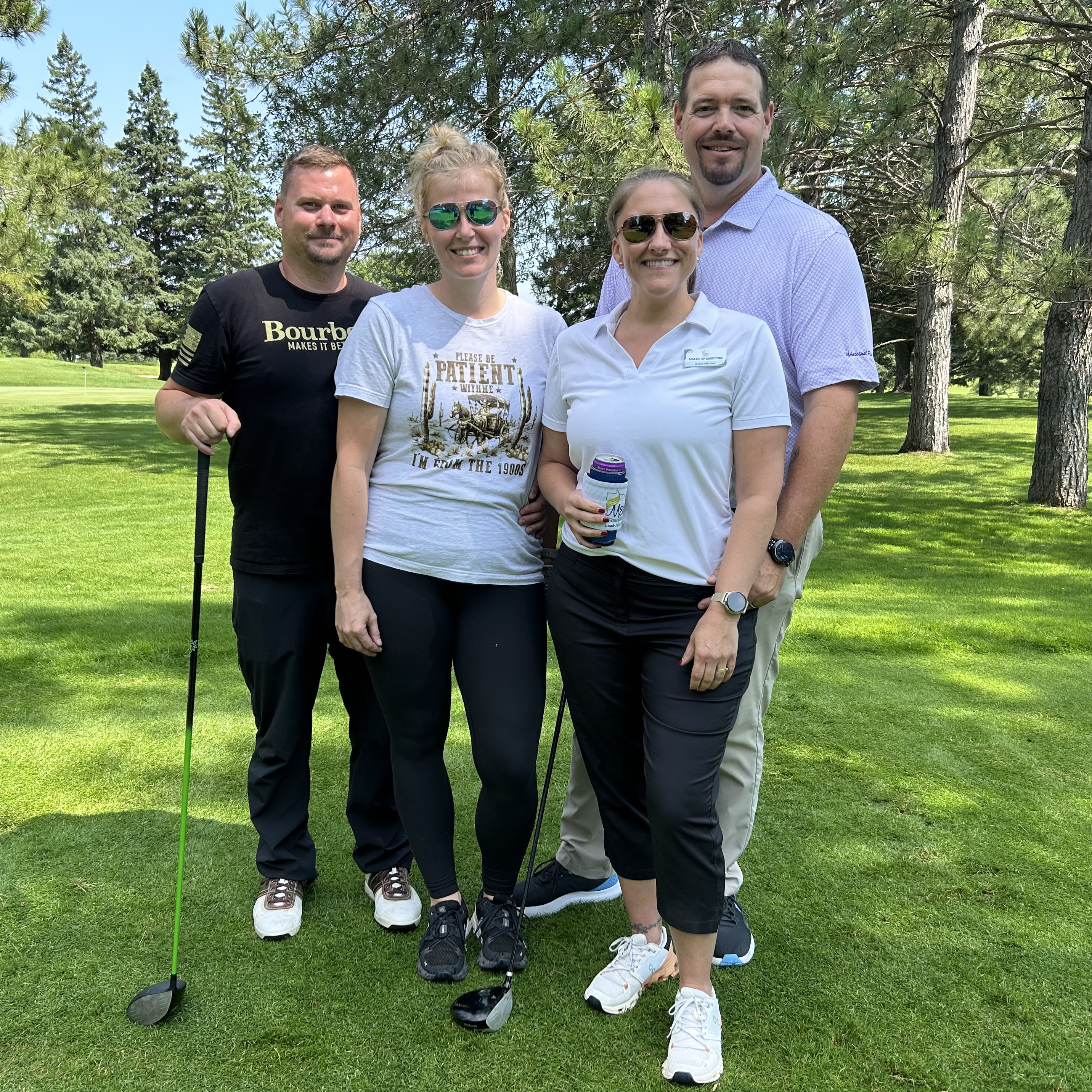 Four golfers, two in sunglasses, pose on the course
