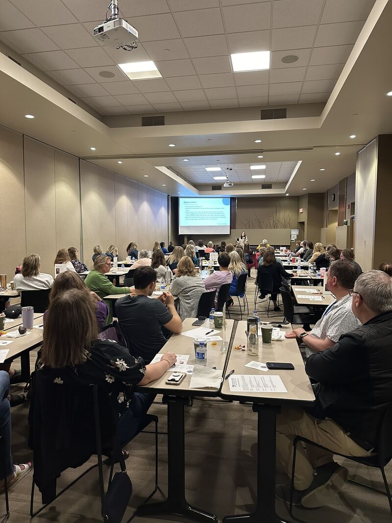 A room full of Cancer Care Conference attendees watch a presentation by a guest speaker in the Oscar Bergos room at M State's Moorhead campus at the 2025 event.