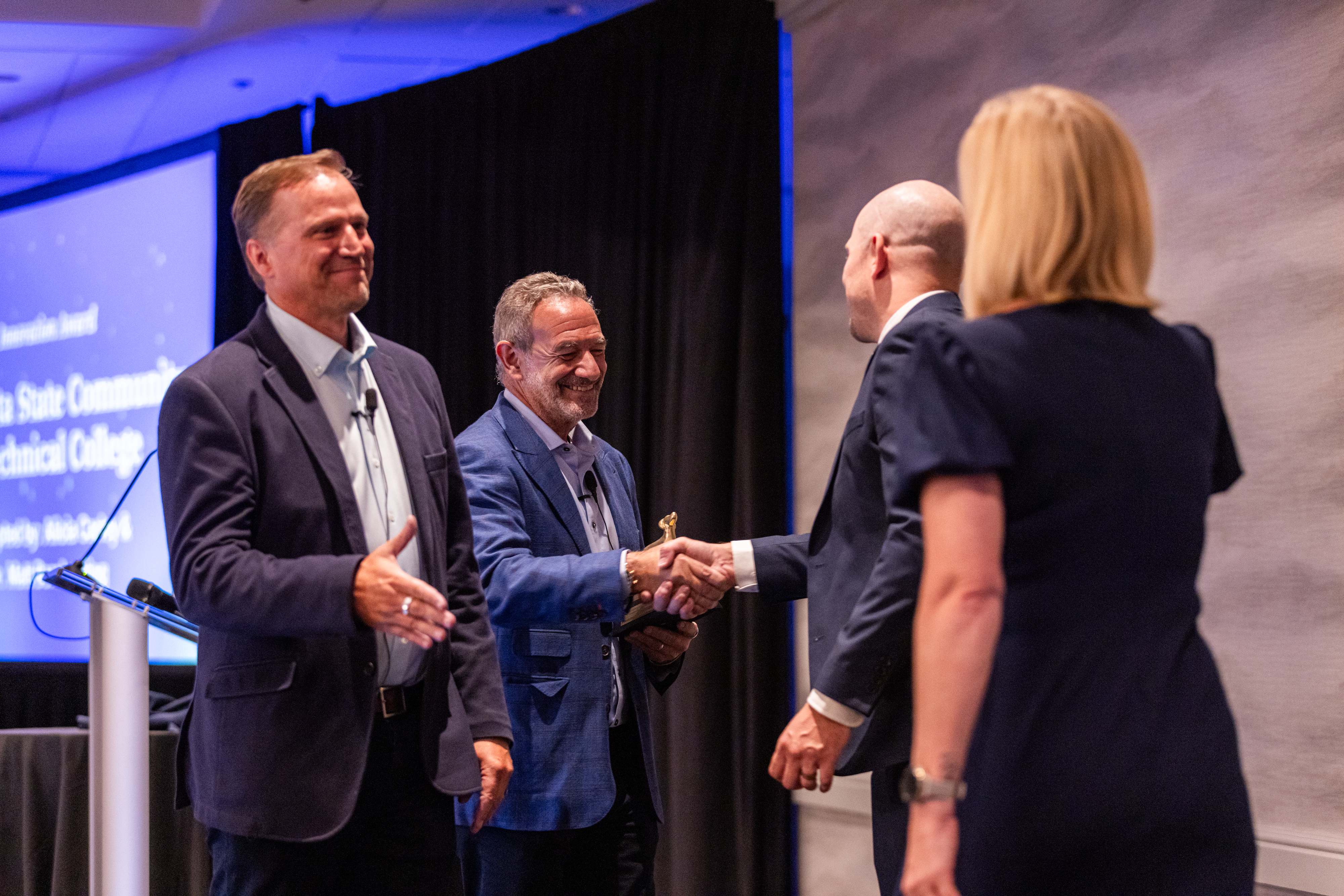 Two Coursedog leaders shake hands with two M State representatives on stage at the 2025 awards ceremony.