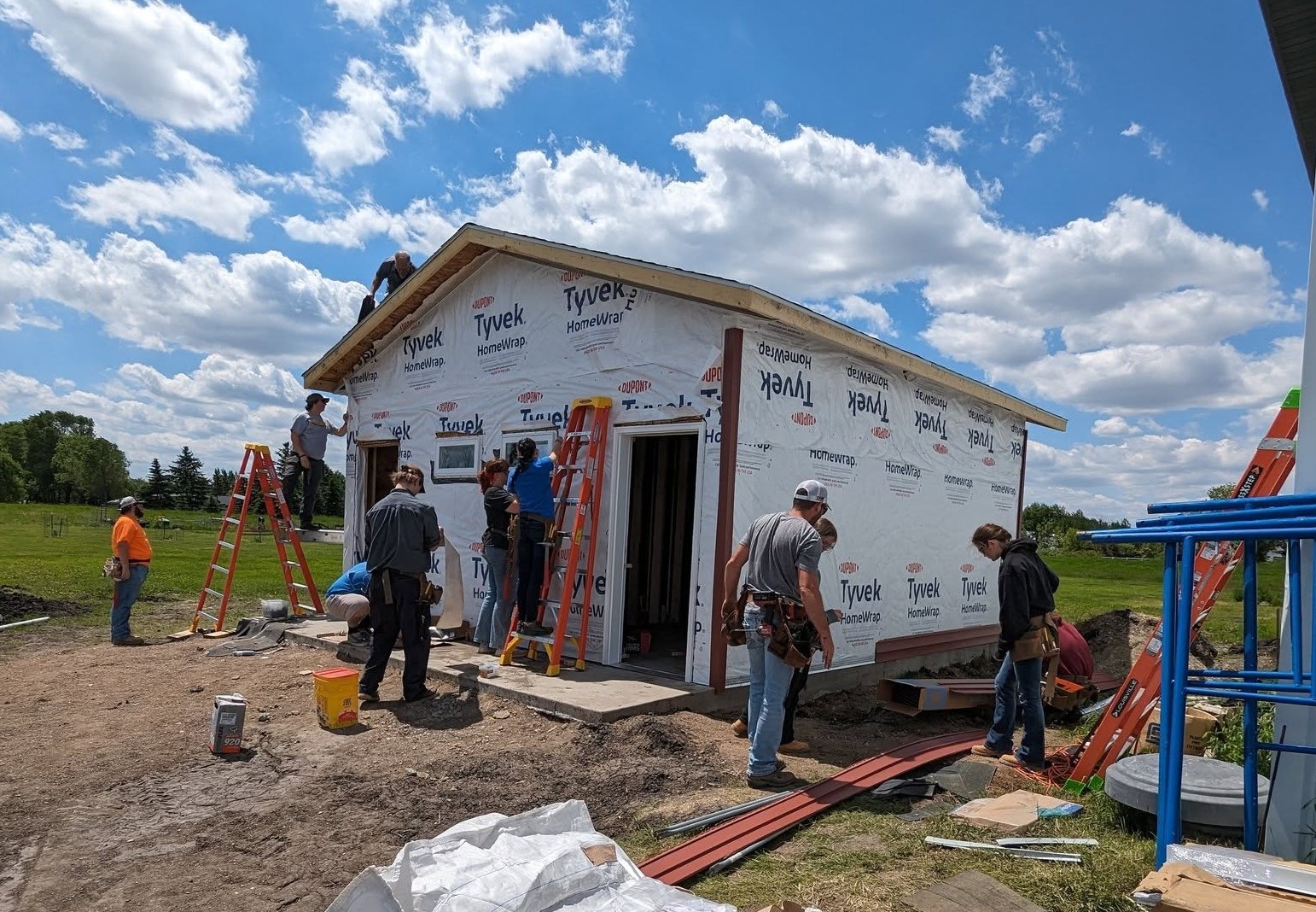 Several students and instructors at the 2024 Herdina Construction Trades Camp are pictured doing various jobs around the site of an under-construction small building.