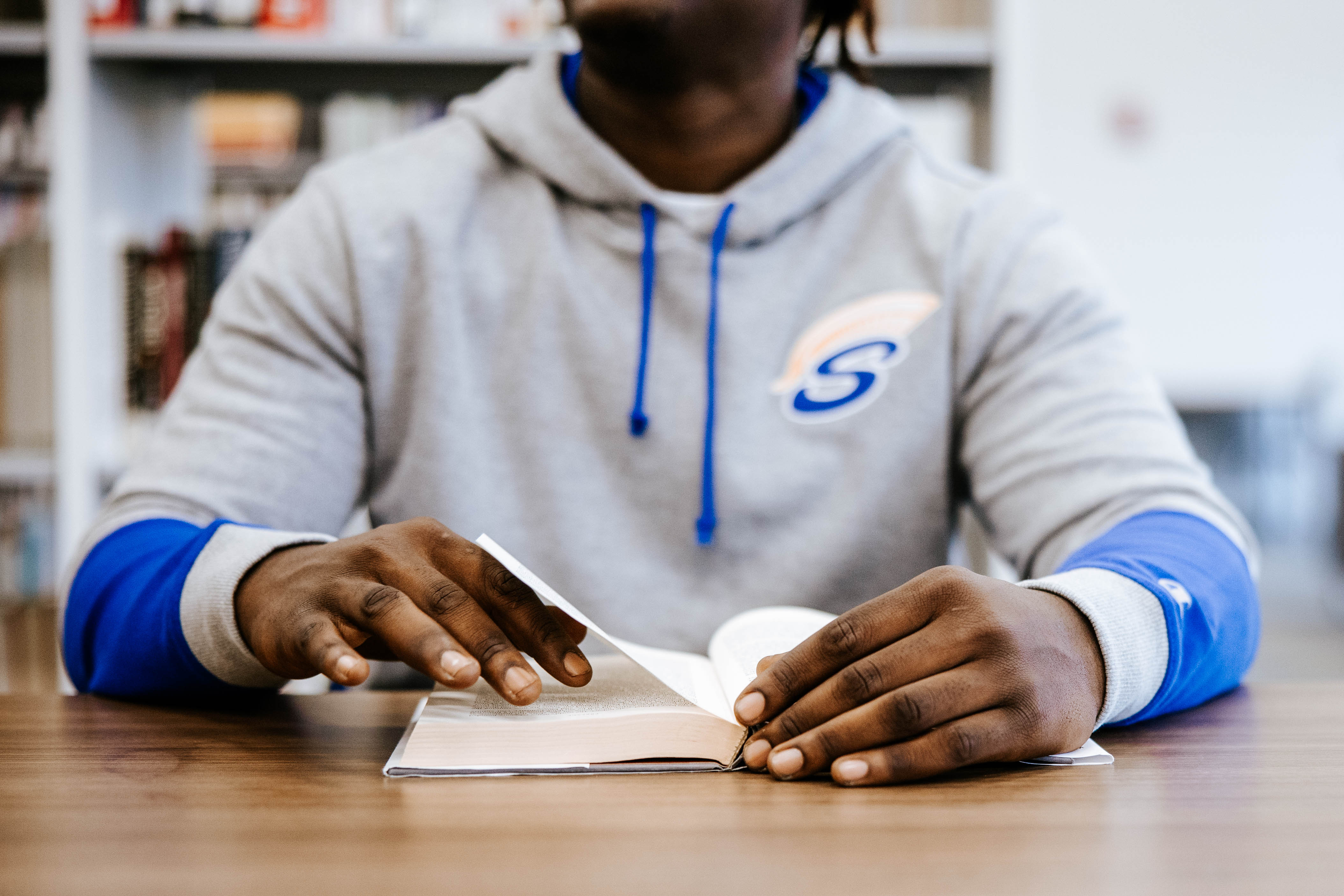A student wearing a Spartan hoodie reads a book at the M State Fergus Falls library.