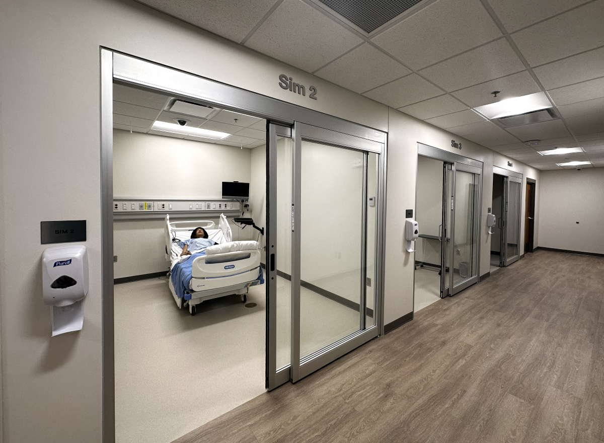 A hallway inside the Health Sciences Simulation Center, with three simulated hospital rooms, with sliding glass doors and white walls.