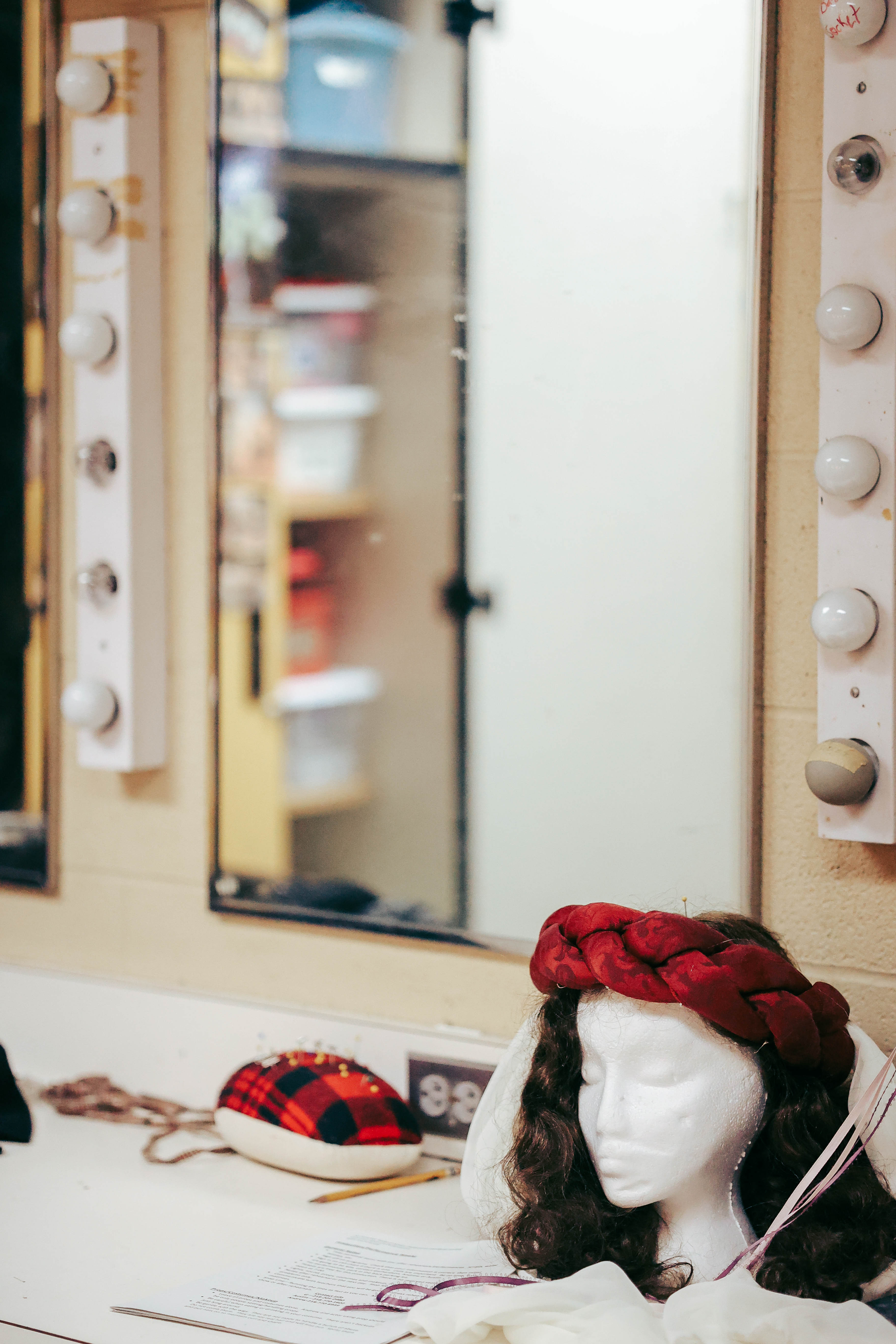 Costume elements sit on a shelf in front of a lighted mirror backstage at the Waage Theatre