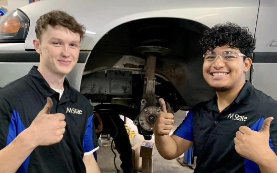 Fix It Forward volunteers give the thumbs up next to a car they fixed up for someone in need