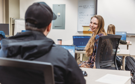 A student looking over her shoulder smiling at the camera with a laptop open in front of her
