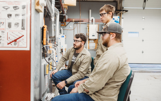 Three HVAC students are looking at a furnace in class