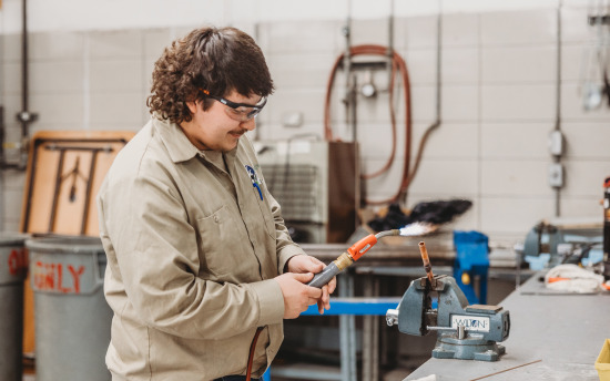 A student from the HVAC program is welding a copper pipe