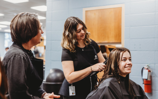 A cosmetology student is giving a haircut while the instructor supervises