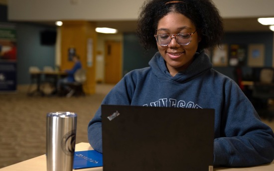 A student in a blue hoodie looks at a laptop