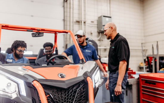 Three students from the Powersports program gathered around a small engine