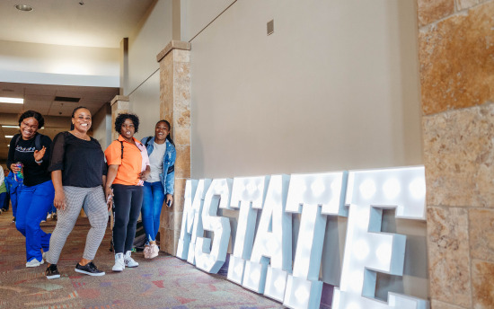 Photo of nursing students surrounding a light up sign that says "M State"