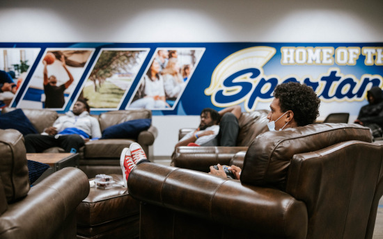 people sitting in leather chairs in front of a home of the Spartans sign