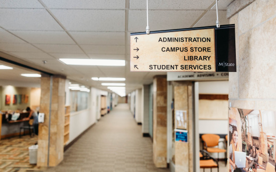 Photo of the interior of M State-Moorhead with a sign pointing directions to administration, campus store and library