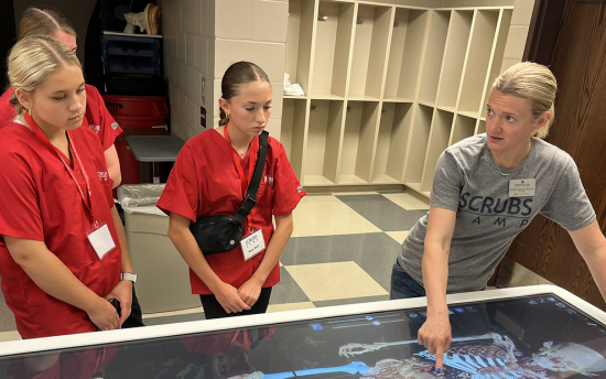 Scrubs camps students and an instructor examine a skeleton image