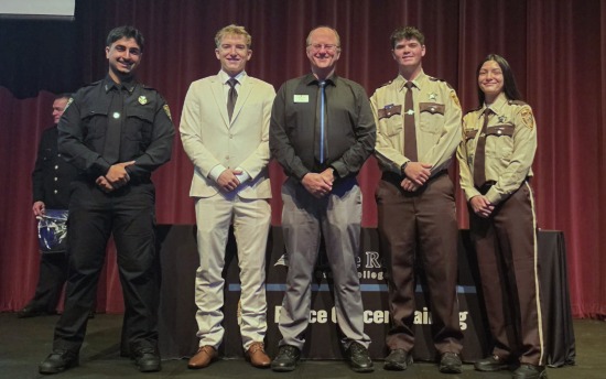 M State Peace Officer Academy graduates Rez Kakayi, Tanner Larson, Carer Jenstead and Destiny Lindgren pose in front of a red curtain following their graduation, with M State Criminal Justice Program Coordinator and Faculty Jeff Nelson, center.