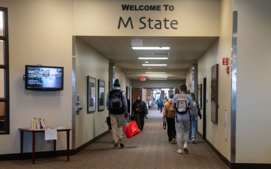 Students walk down a hallway under a "Welcome to M State" sign on the M State Moorhead campus