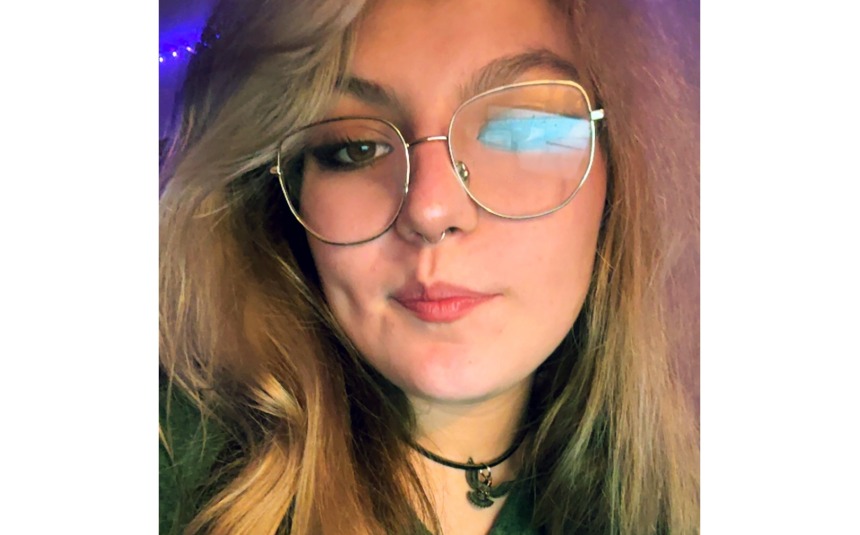 Head shot of a woman with blond hair and silver-rimmed glasses, with a closed-mouth smile and choker-style necklace