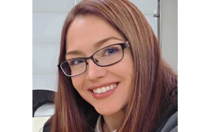 Head shot of a woman with long straight brown hair and black-rimmed glasses, smiling