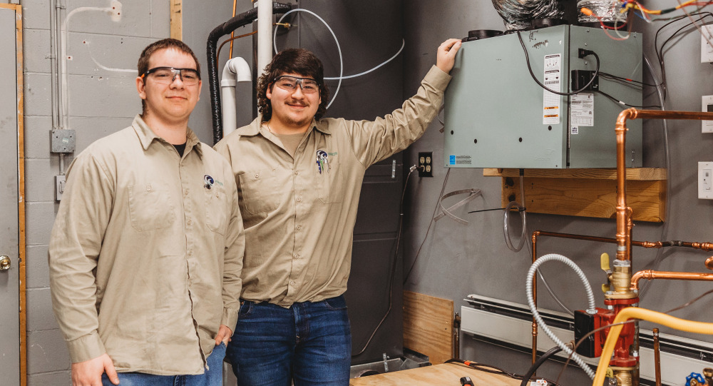 Two men smiling in front of metal hvac box