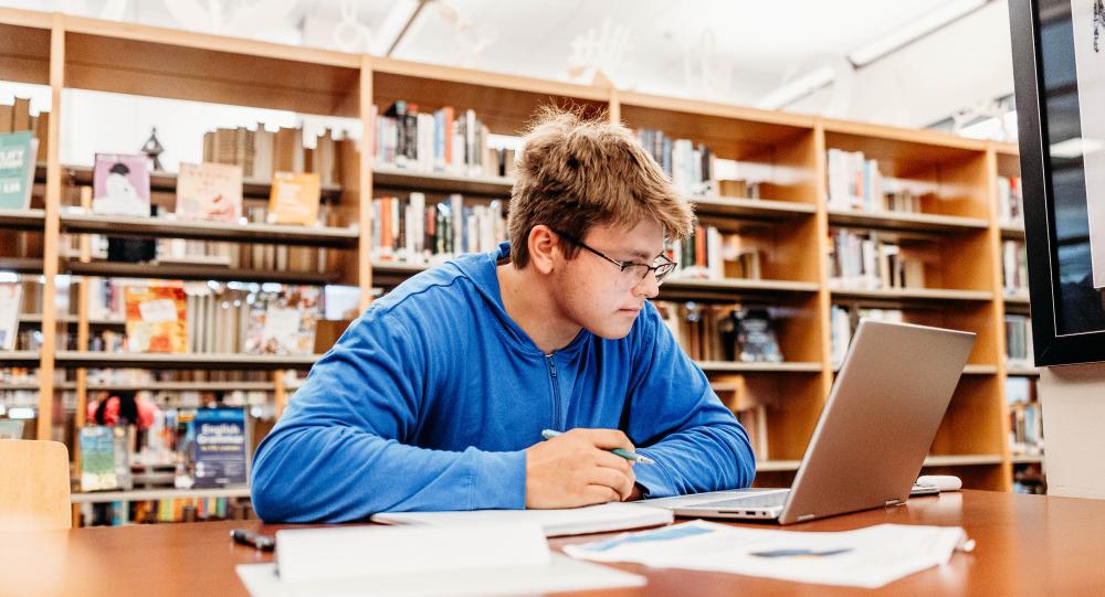 man in library sitting at table working at computer