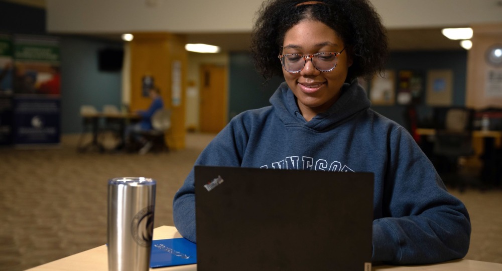 A student in a blue hoodie looks at a laptop