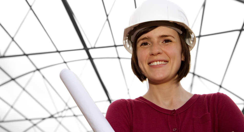 A person in a red sweater and white hard hat holds rolled-up papers