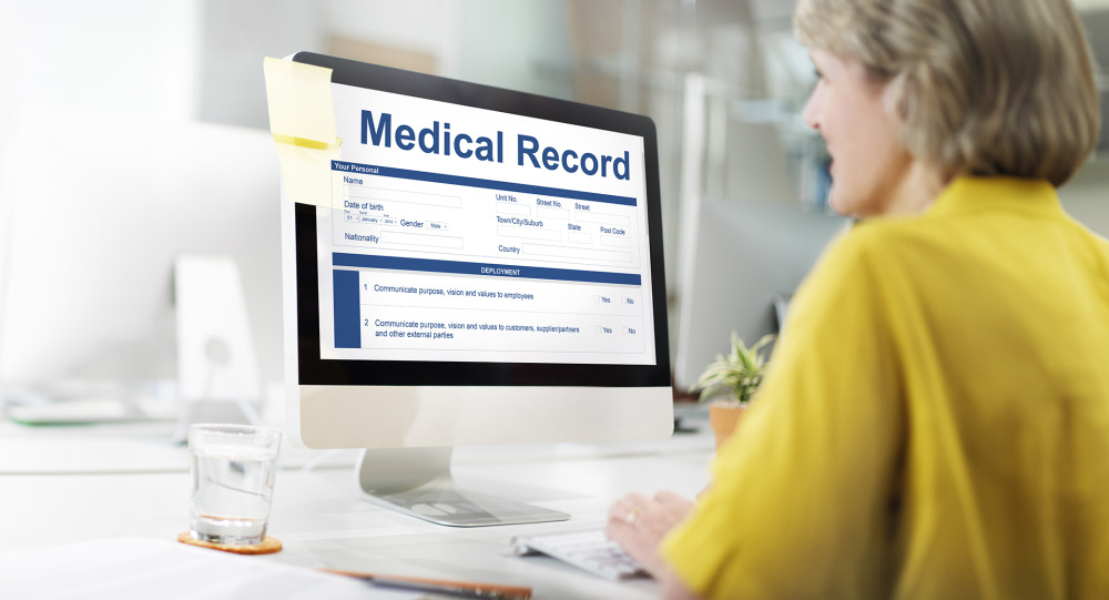 A person in yellow examines medical records on a computer monitor