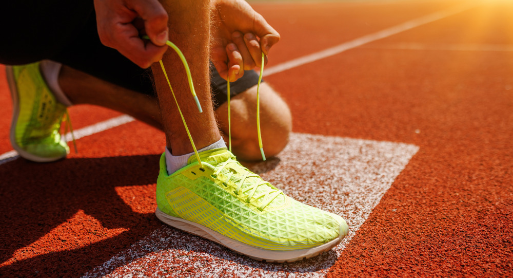A person tying their athletic shoe on a track