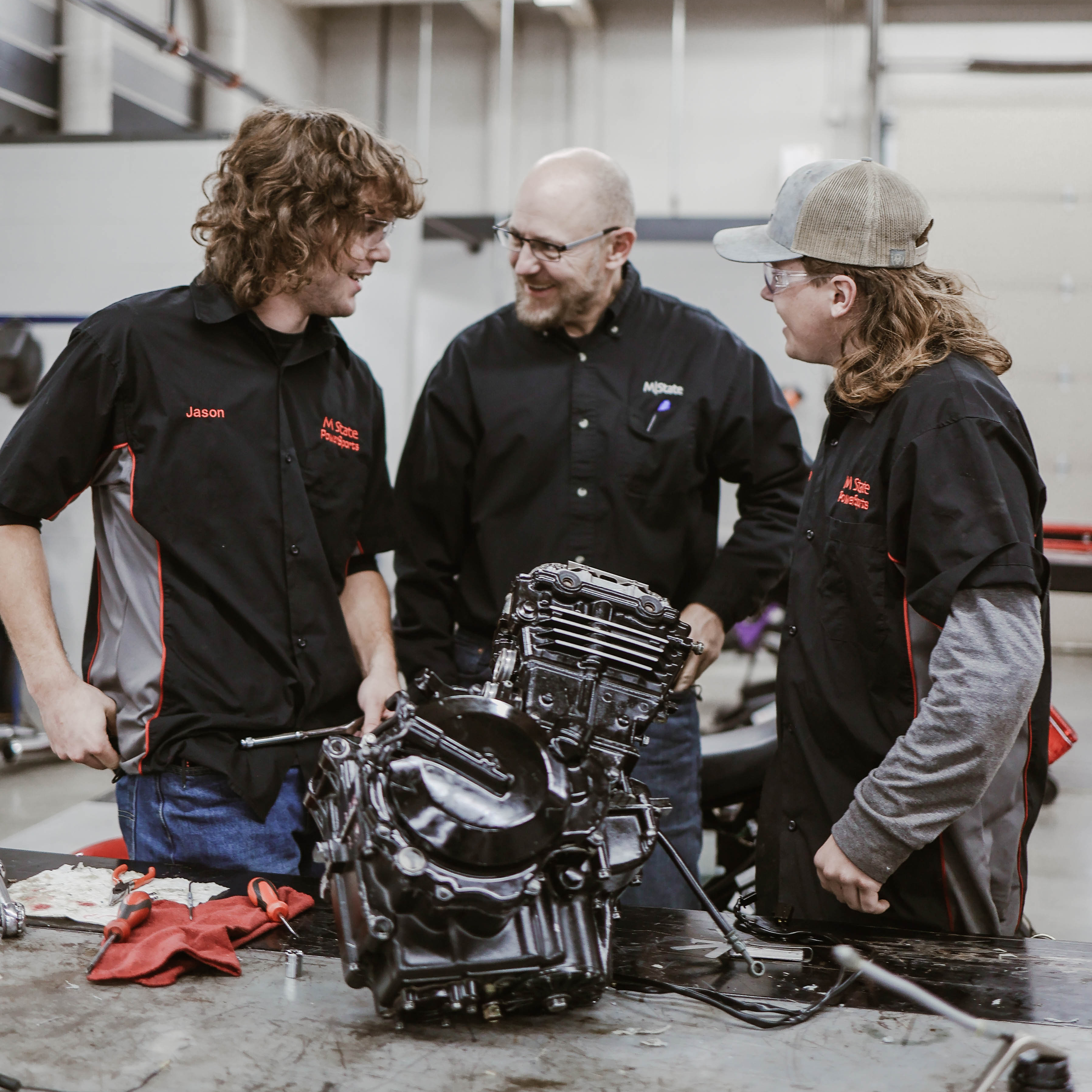 Kent Reisenauer and two PowerSports Technology students laugh during a class in the early 2020s.