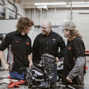 Kent Reisenauer and two PowerSports Technology students laugh during a class in the early 2020s.